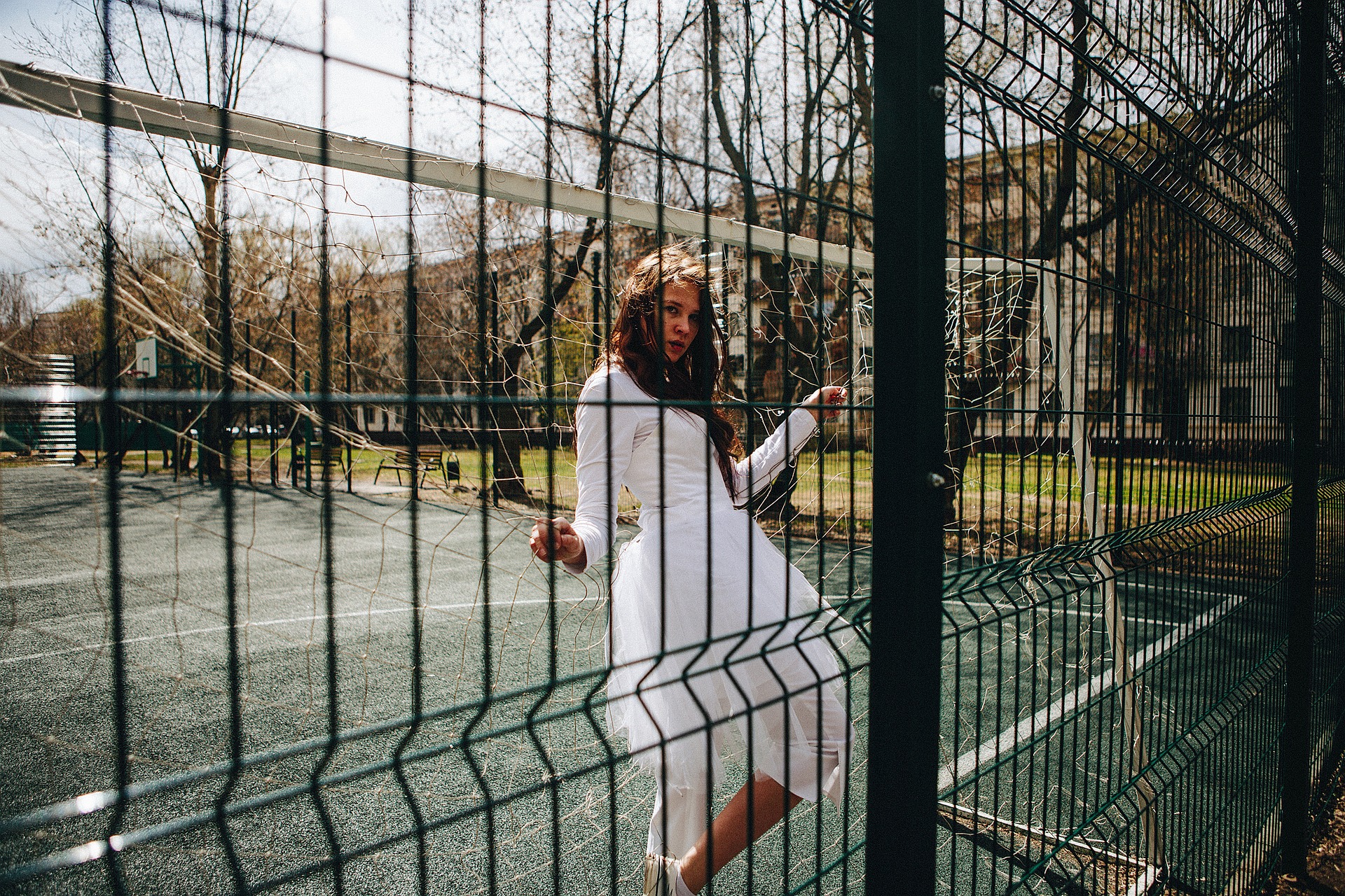 Frau in weißem Kleid steht hinter einem Zaun auf einem Tennisplatz