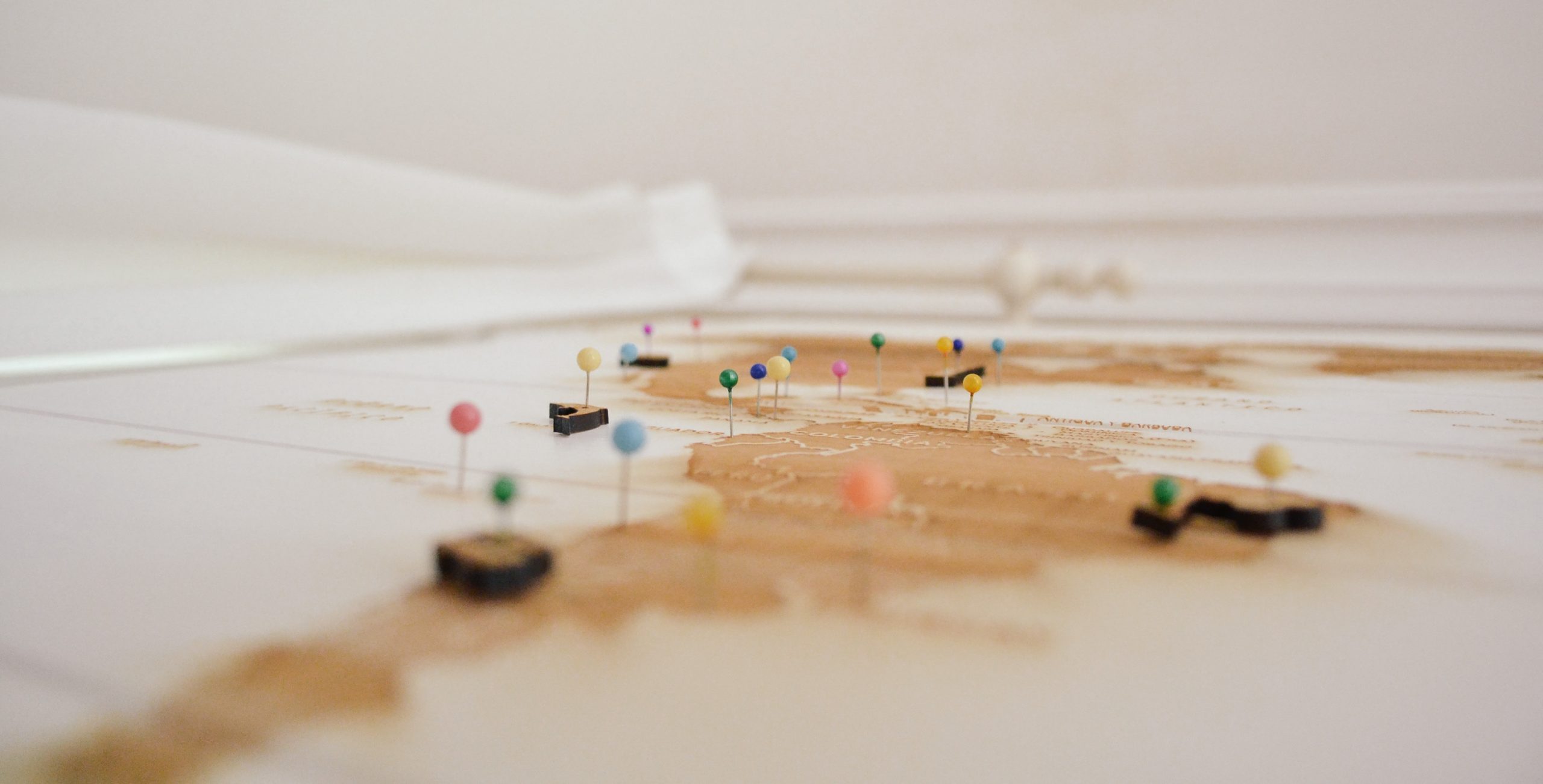 Blick auf eine weiß-beige Landkarte mit bunten Pins, die verschiedene Orte markieren – Symbol für Erinnerungen und Reisen.