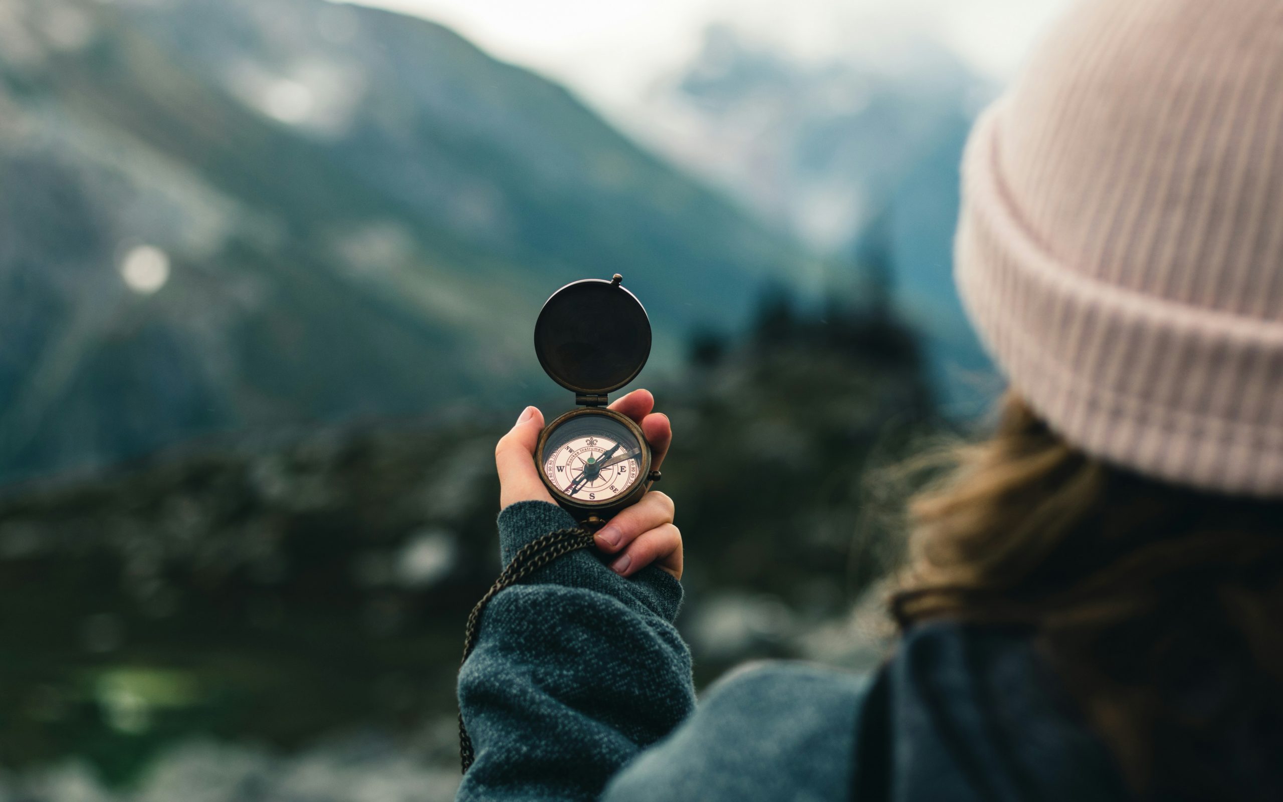 Ein Mensch mit Mütze hält einen Kompass in der Hand, den Blick auf eine weite, neblige Landschaft gerichtet – zwischen Orientierung und Zweifel
